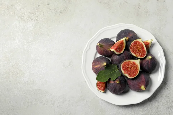 Whole and cut ripe figs with leaf on light table, top view. Space for text