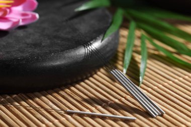 Bambu hasırının üzerinde akupunktur iğneleri ve spa taşı, yakın plan.
