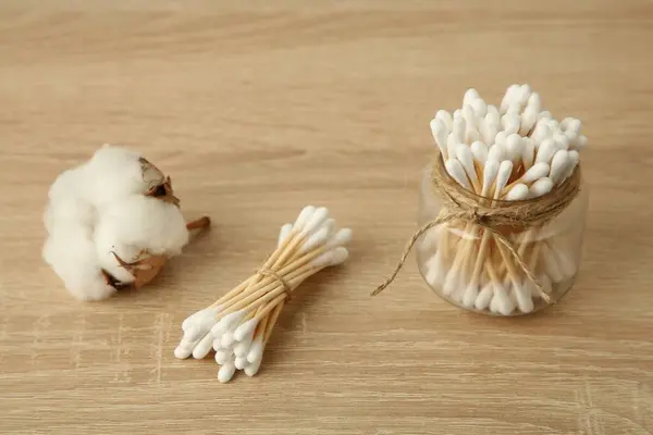 Cotton swabs and flower on wooden table