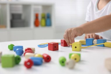 Motor beceri geliştirme. Küçük çocuk ahşap parçalarla oynuyor ve beyaz masa içerisindeki iplik aktivitesi için, yakın plan.