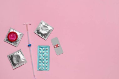 Doğum kontrol tercihi. Pembe arka planda haplar, prezervatifler ve rahim içi cihazlar. Metin için boşluk