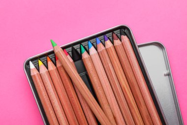 Pembe arka planda renkli pastel kalemlerle dolu bir kutu, üst manzara. Malzemeler çiziliyor