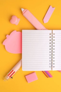 Düz kompozisyon, açık defter ve sarı arka planda farklı okul kırtasiyesi, metin için boşluk. Okula geri dön.