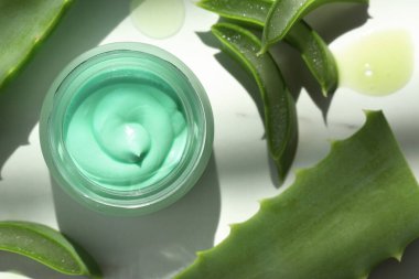 Kremalı kavanoz ve beyaz masa üzerinde aloe yaprakları, düz yatıyordu
