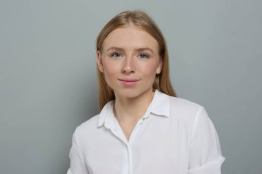 Gri arka planda beyaz gömlekli güzel bir genç kadının portresi.