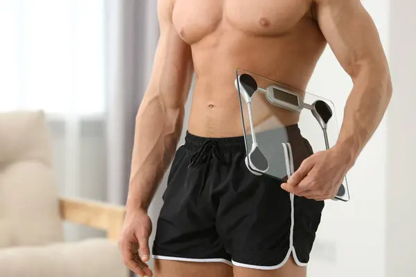 Athletic man holding scales at home, closeup. Weight loss concept