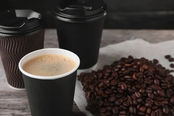 Coffee to go. Paper cups with tasty drink and roasted beans on table, closeup. Space for text