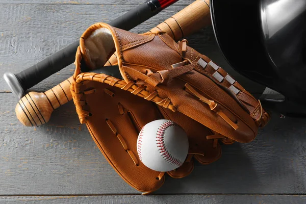 Baseball glove, bats, ball and batting helmet on grey wooden table, closeup