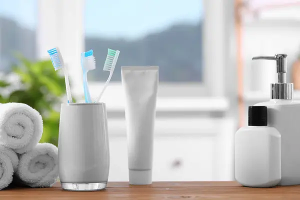 Plastic toothbrushes in holder, cosmetic products and towels on wooden table indoors