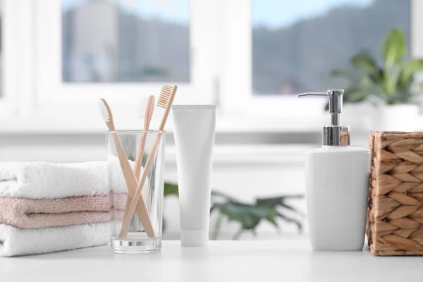Bamboo toothbrushes in holder, cosmetic product and towels on white table indoors