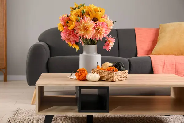 Beautiful autumn bouquet and small pumpkins on wooden table near sofa in room