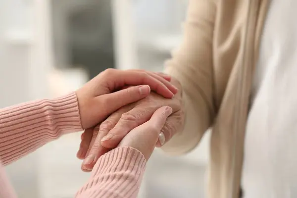 Trust and support. Woman with her dad joining hands indoors, closeup
