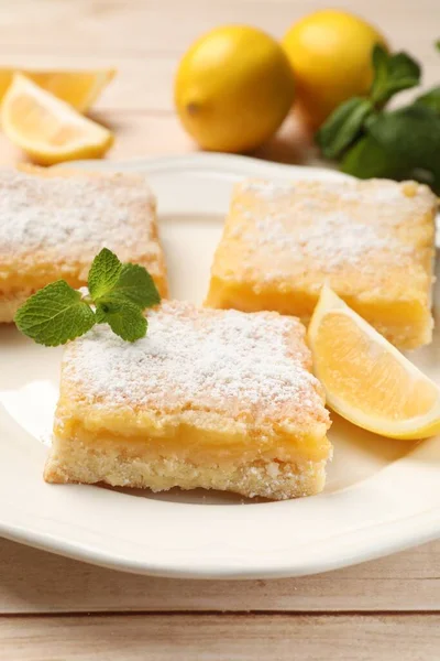 Tasty lemon bars with powdered sugar and mint on wooden table, closeup