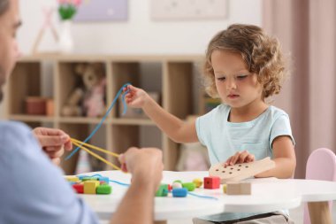 Motor beceri geliştirme. Baba ve küçük kızı beyaz masada ahşap bağcıklı oyuncaklarla oynuyor.