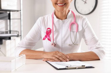İçerideki beyaz masada steteskoplu ve pembe kurdeleli bir doktor, yakın plan. Göğüs kanseri farkındalığı
