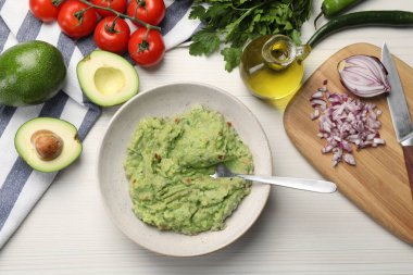 Lezzetli guacamole kasede ve malzemeler beyaz ahşap masada, düz yerde.