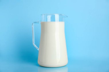 Açık mavi arkaplanda bir sürahi taze süt