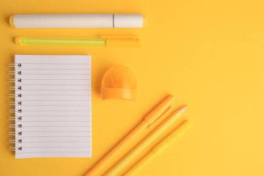 Düz kompozisyon, açık defter ve sarı arka planda farklı okul kırtasiyesi, metin için boşluk. Okula geri dön.