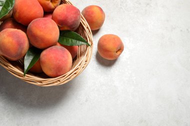 Hasır sepetin içinde taze şeftali ve yapraklar açık dokulu masada, düz yerde. Metin için boşluk
