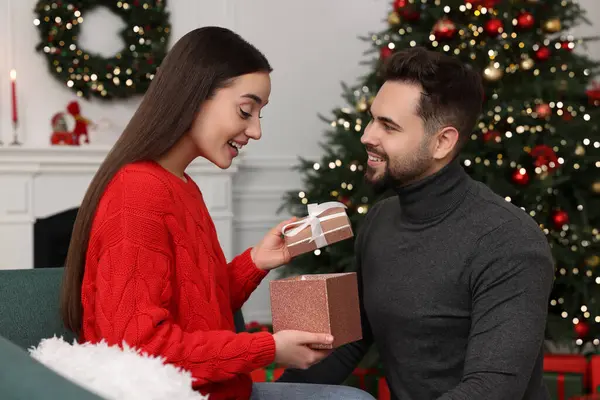 Surprised young woman opening Christmas gift from her boyfriend at home