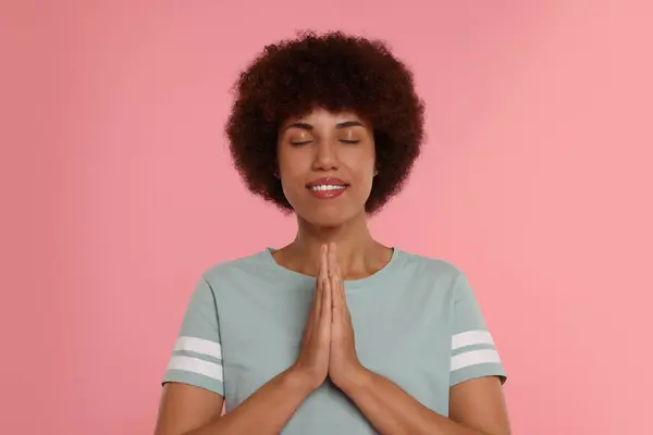 Woman with clasped hands praying to God on pink background