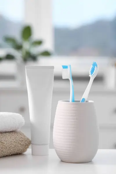Plastic toothbrushes in holder, toothpaste and towels on white table indoors