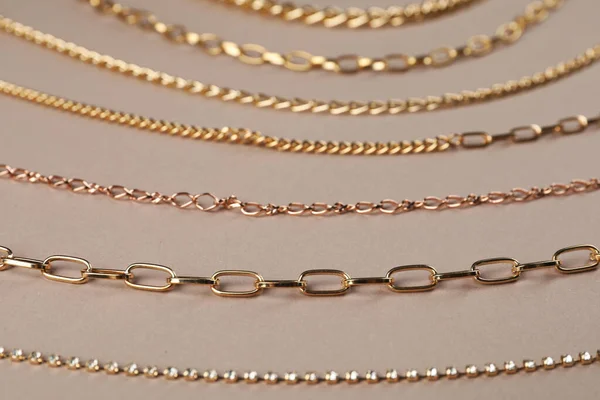 Different metal chains on light brown background, closeup. Luxury jewelry