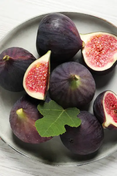 Whole and cut ripe figs with leaf on white wooden table, top view