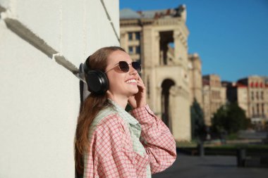 Kulaklıklı gülümseyen kadın bina yakınlarında müzik dinliyor.