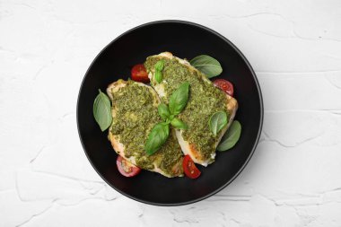 Pesto soslu leziz tavuk göğsü, beyaz desenli masada domates ve fesleğen.