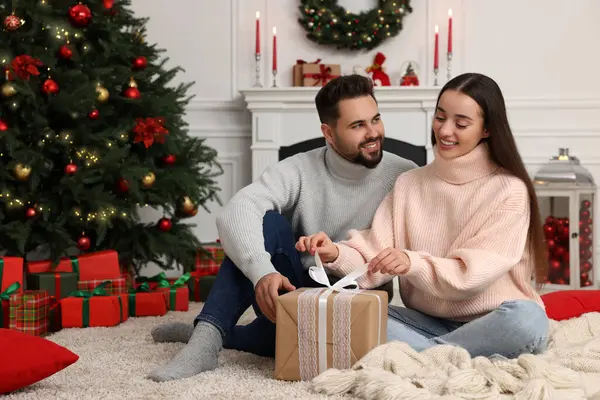 Happy young woman opening gift from her boyfriend in room decorated for Christmas