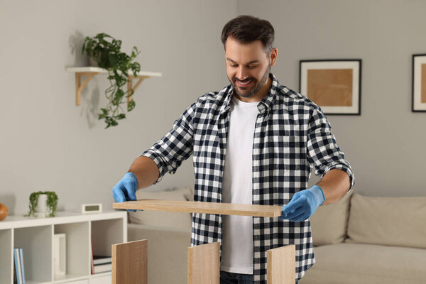Мужчина собирает деревянную мебель в гостиной
