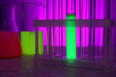 Masanın üzerinde mor arkaplana karşı parlak sıvılar bulunan laboratuvar camları, yakın plan.