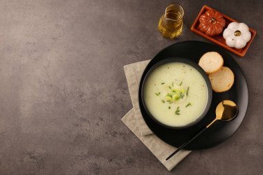 Lezzetli bir kase pırasa çorbası, gri masada kaşık ve ekmek, düz yatak. Metin için boşluk