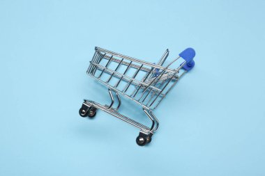 Açık mavi arka planda küçük metal alışveriş arabası.
