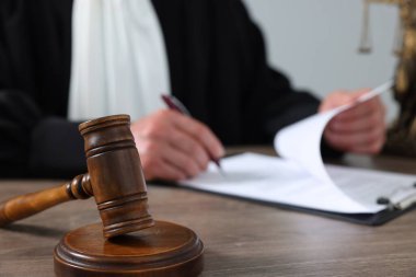 Tahta masada, açık gri arkaplanda yazılı kağıtlarla hakim, yakın plan.
