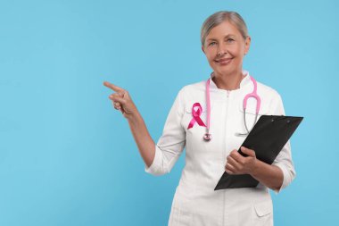 Pembe kurdeleli doktor, not panosu ve açık mavi arka planda steteskop, mesaj için yer. Göğüs kanseri farkındalığı