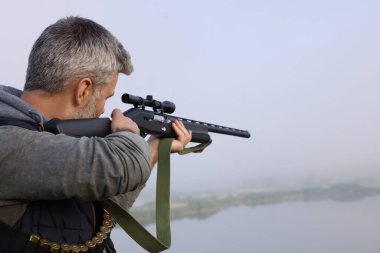 Açık havada göl kenarında av tüfeği tutan bir adam. Metin için boşluk