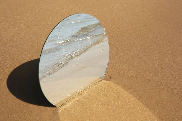 Round mirror reflecting sea on sandy beach