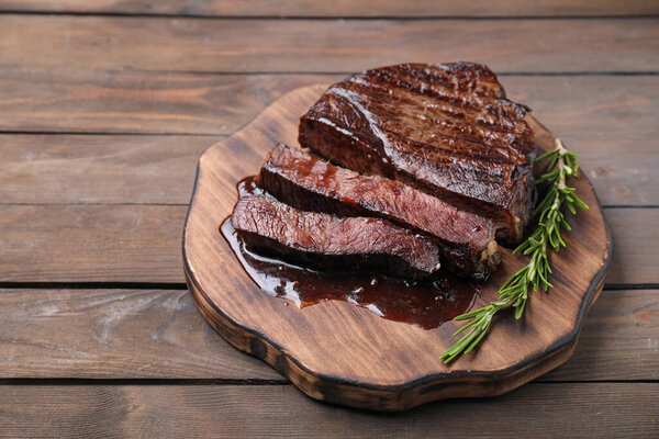 Delicious grilled beef meat and rosemary on wooden table, closeup. Space for text