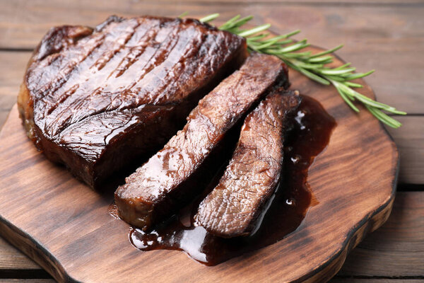 Delicious grilled beef meat and rosemary on wooden table, closeup