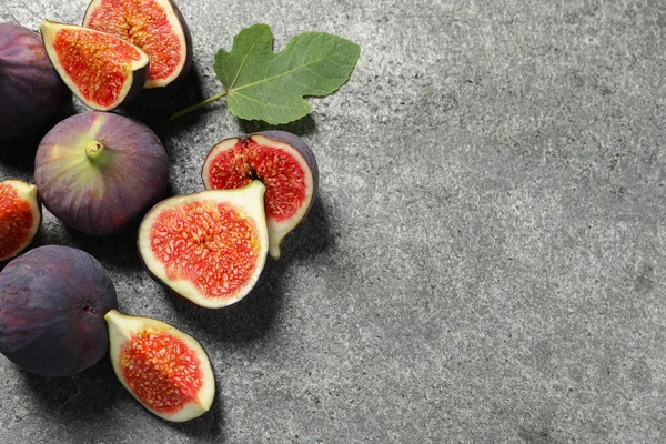 Whole and cut ripe figs with leaf on grey textured table, flat lay. Space for text
