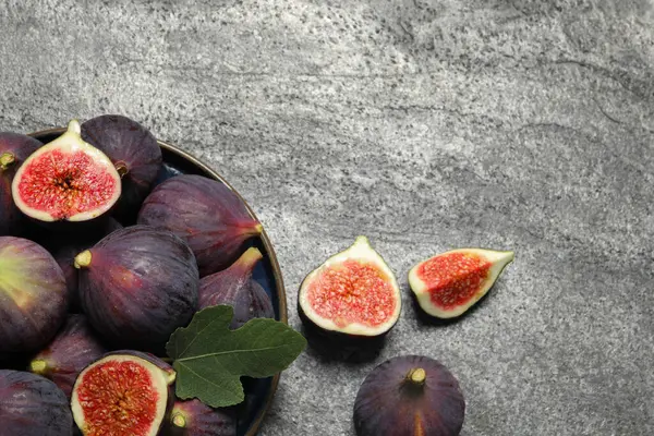 Whole and cut ripe figs with leaf on light grey textured table, flat lay. Space for text