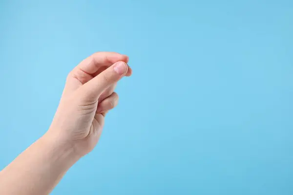 Woman holding something in fingers on light blue background, closeup. Space for text