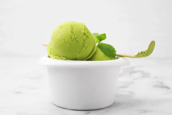 Tasty matcha ice cream in bowl and spoon with powder on white marble table