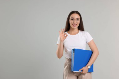 Dizini olan mutlu kadın açık gri arkaplanda iyi niyet göstergesi gösteriyor, metin için boşluk