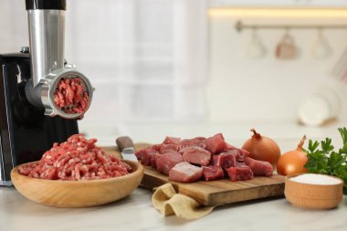 Elektrikli et öğütücü. Mutfaktaki beyaz mermer masaya sığır eti ve ürünler.