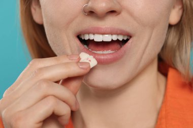 Açık mavi arka planda, ağzına balonlu sakız yapıştıran kadın, yakın plan.