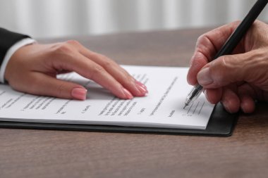 Yönetici, içerideki ahşap masaya imza atması gereken yeri gösteriyor.
