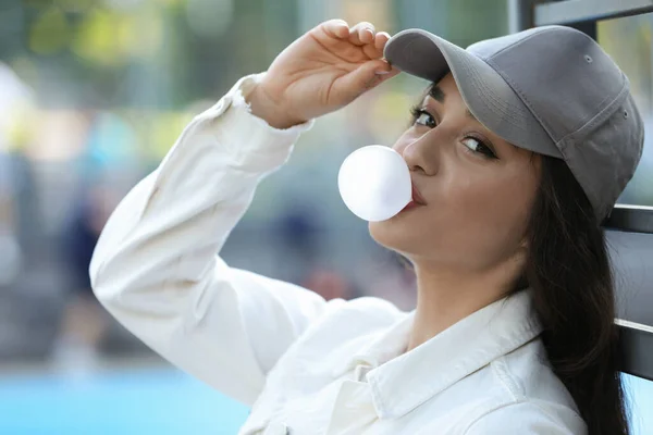Beautiful young woman blowing bubble gum outdoors